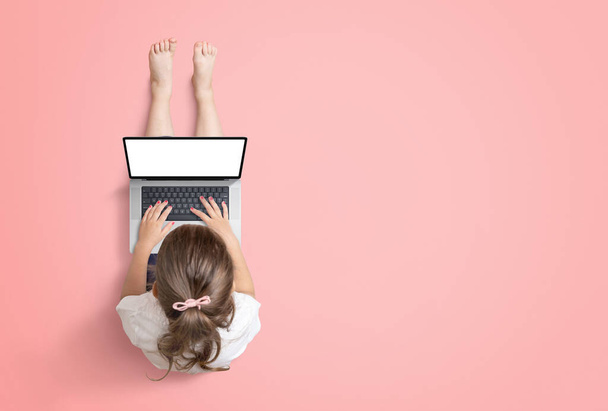 Little girl works on a laptop computer. View from above. Isolated screen for mockup, website or game promotion. Copy space beside on red background - Fotoğraf, Görsel