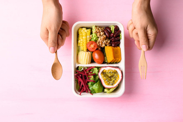 Čerstvý zeleninový salát v biologicky rozložitelné míse s rukou na růžovém pozadí, zdravé veganské jídlo - Fotografie, Obrázek