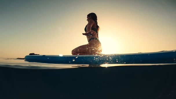 Woman in bikini does bodyweight exercises on a paddle sup board - Foto, imagen