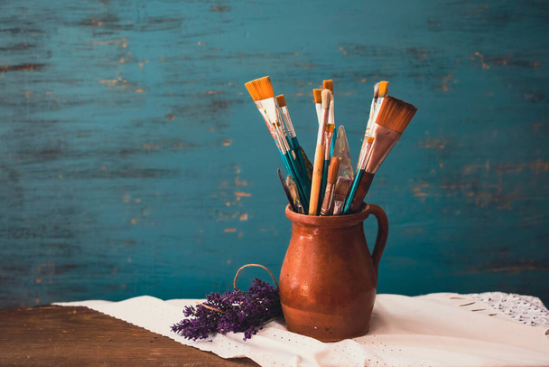 Still life of paint brushes  in clay jug an lavender flower on vintage turquoise background - Photo, image