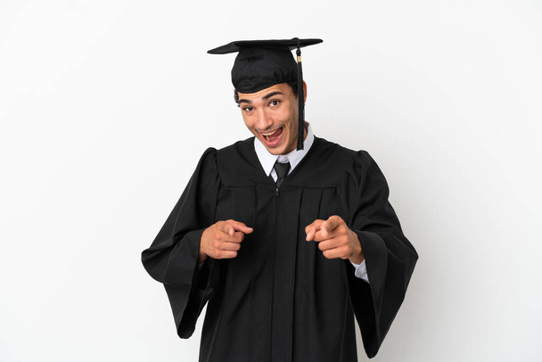 Молодой выпускник университета на изолированном белом фоне указывая на фронт и улыбаясь - Фото, изображение