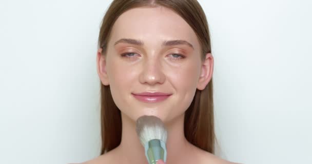 The face of a woman doing her makeup with a powder brush. The concept of cosmetic skin care. - Záběry, video