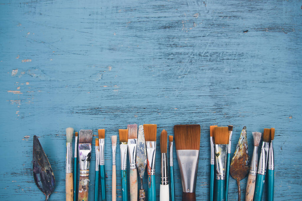 Artistic art supply utensils with paintbrushes on turquoise wooden background with copy space. Flat lay photo - Foto, Bild