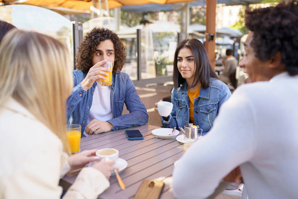 Grupo multiétnico de amigos tomando una copa juntos en un bar al aire libre. Los jóvenes se divierten. - Foto, Imagen