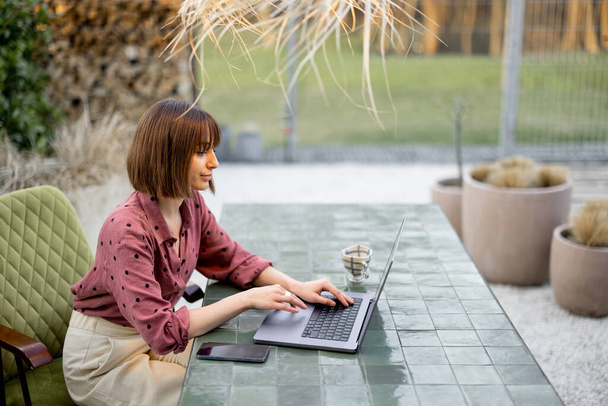 Młoda kobieta pracuje na laptopie w ogrodzie. Pojęcie pracy zdalnej z wygodnego biura domowego lub pracy w czasie wakacji - Zdjęcie, obraz