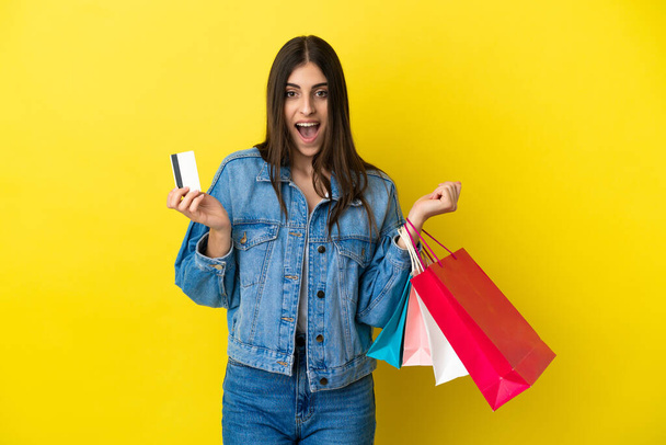 Young caucasian woman isolated on blue background holding shopping bags and surprised - Foto, Imagem