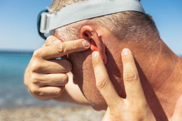 Mature man putting silicone ear plugs, surfers earplugs, swim plugs - Photo, Image
