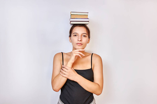 Το κορίτσι κρατάει βιβλία στο κεφάλι της. Έννοια της σκληρής κατάρτισης. - Φωτογραφία, εικόνα