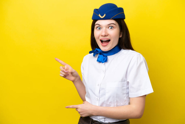Airplane stewardess Russian woman isolated on yellow background surprised and pointing side - Foto, Imagen