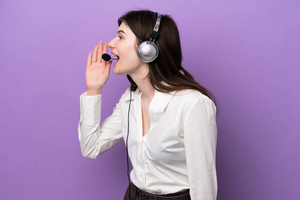 Telemarketer Russian woman working with a headset isolated on purple background shouting with mouth wide open to the lateral - Photo, image