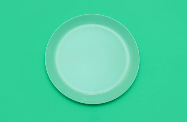 Green round empty plate on a green background. Top view. - Φωτογραφία, εικόνα