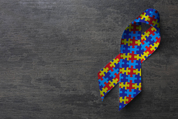World Autism Awareness Day. Colorful puzzle ribbon on grey stone background, top view with space for text - Foto, imagen