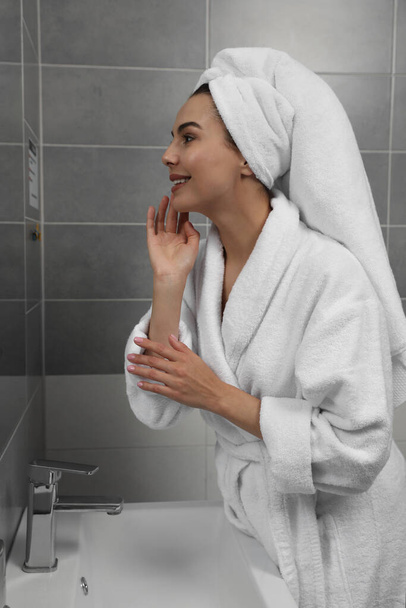 Beautiful young woman in bathrobe with towel on head near mirror at home - Фото, зображення