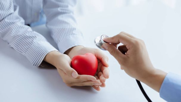 A doctor uses a stethoscope with a fake heart in the patient's hand, treating the disease from a medical professional and giving treatment on the spot. Concepts of medical treatment and specialists. - Foto, Bild