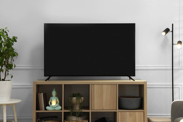 Modern TV on cabinet, lamp and beautiful houseplants near white wall indoors. Interior design - Fotó, kép