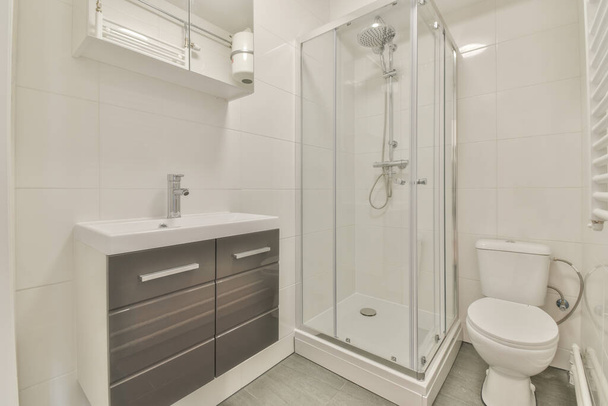 現代的なアパートの光のトイレでシンクとミラーの近くに位置ガラスドア付きのタイル張りのシャワーキャビン - 写真・画像