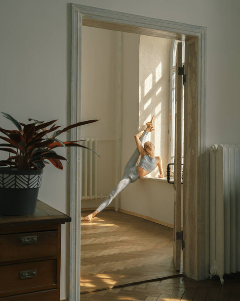 Фитнес, йога, растяжка и здоровый образ жизни концепция - молодая женщина делает упражнения у окна дома - Фото, изображение