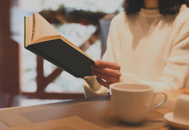 Woman with coffee reading book at wooden table, closeup - Foto, Imagen