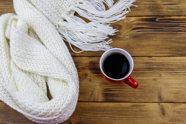 Knitted white scarf and cup of coffee on wooden table. Top view. Winter cozy concept - Foto, Imagem