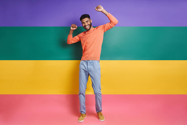 Full length of happy African man gesturing while standing against colorful background - Foto, immagini