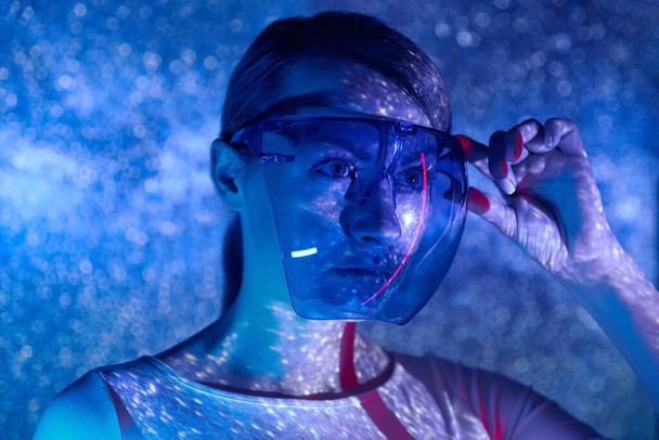 Confident young woman adjusting futuristic glasses against colorful background - Foto, Bild