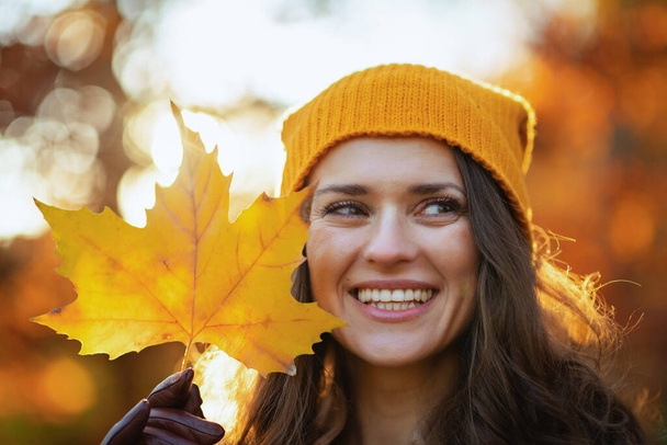 Hello autumn. happy young female in brown coat and yellow hat with autumn yellow leaves outside in the city park in autumn. - Fotó, kép