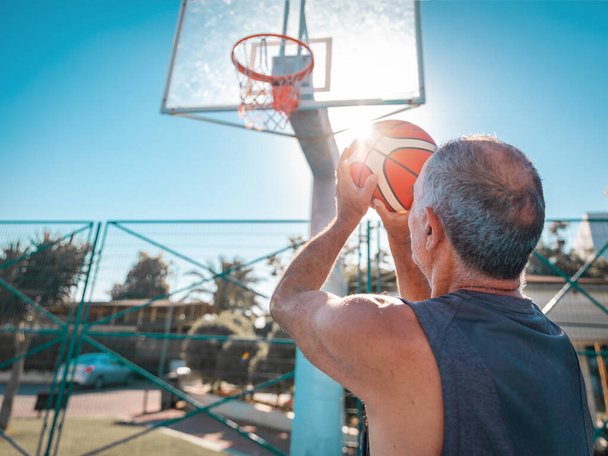 60-jähriger Basketballspieler schießt Körbe im Freien. Älterer Amateur wirft Ball in Korb - Foto, Bild