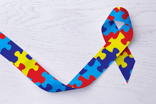 World Autism Awareness Day. Colorful puzzle ribbon on white wooden background, top view - Foto, imagen