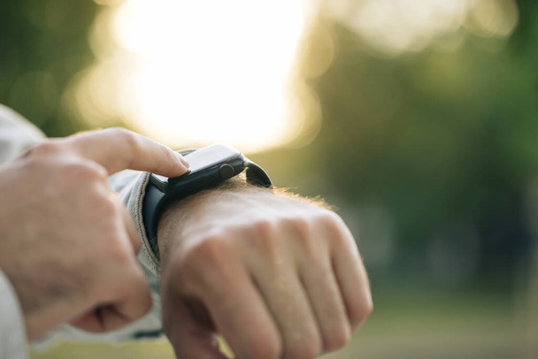 Smart watch. Smart watch on a mans hand outdoor. Mans hand touching a smartwatch. Close up shot of males hand uses of wearable smart watch at outdoor in sunset. - Foto, Imagem