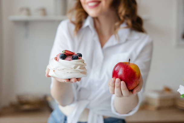 Girl holding a cake in one hand and an apple in the other while standing in the kitchen. High quality photo - Fotó, kép