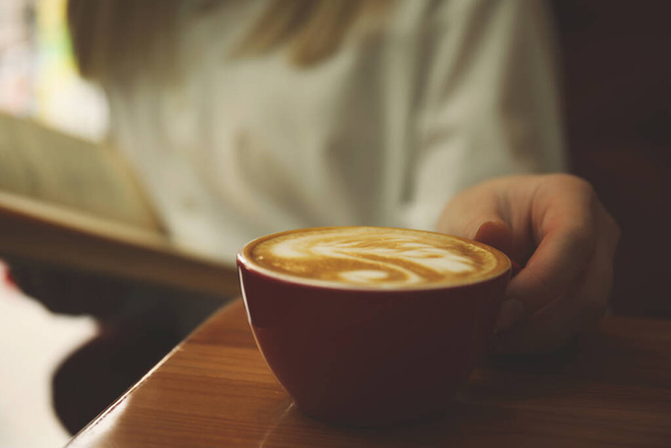 Woman with coffee reading book indoors, focus on cup - Φωτογραφία, εικόνα