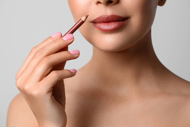 Young woman applying beautiful nude lip pencil on light grey background, closeup - Foto, immagini