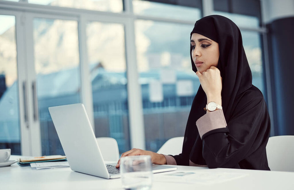uma atraente jovem mulher de negócios árabe trabalhando em seu laptop no escritório. - Foto, Imagem