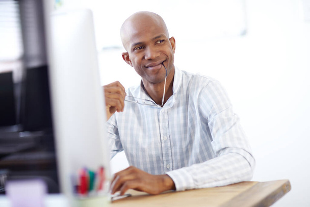 a thougtful-looking african american designer sitting in his chair in front of a desktop computer in the office. - Photo, Image