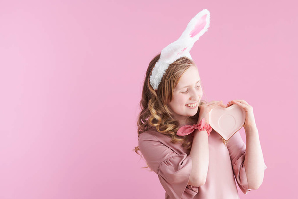 happy modern girl with long wavy blond hair with heart shape saucer and bunny ears against pink background. - Zdjęcie, obraz