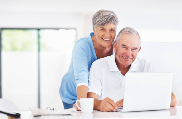 Porträt eines lächelnden reifen Paares mit Laptop zu Hause. - Foto, Bild