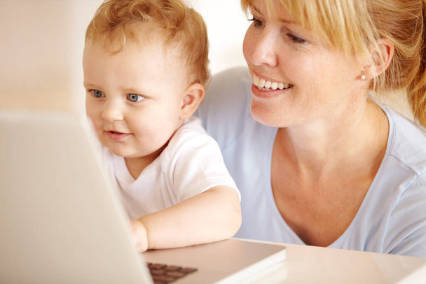 Bela mãe ajudando seu bebê menino tipo em seu computador portátil. - Foto, Imagem