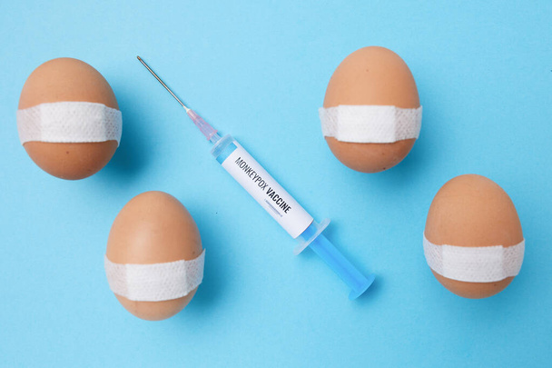 flatlay with monkeypox vaccine syringe and vaccinated eggs with medical patch on blue background. - Fotografie, Obrázek