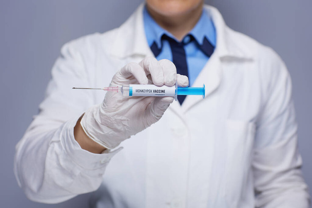 Closeup on modern medical doctor woman in white medical robe with monkeypox vaccine syringe against grey background. - Фото, зображення
