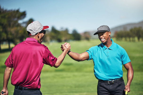dwóch wesołych młodych golfistów biorących udział w uścisku dłoni po świetnym strzale na polu golfowym. - Zdjęcie, obraz