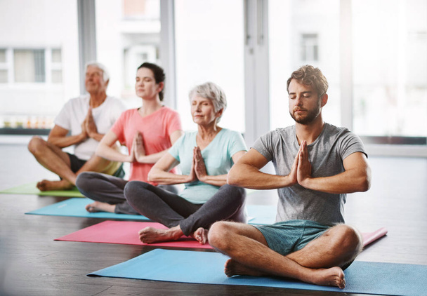 Full length shot of a group of people meditating while practicing yoga. - Photo, image