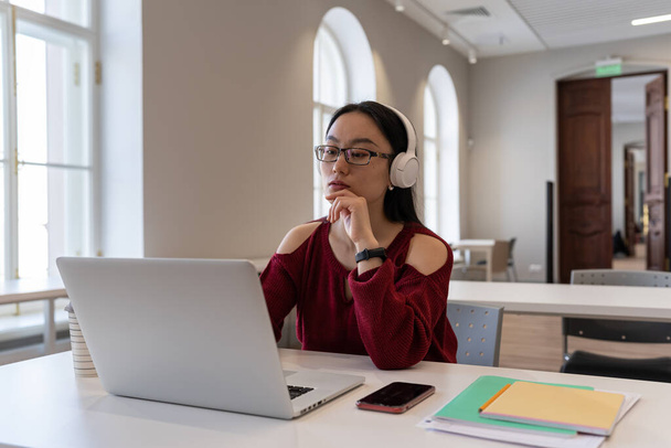 Орієнтована азіатська студентка носить навушники дивитися на ноутбук онлайн-вебінар або навчальний курс. Серйозна тисячолітня китайська жінка, яка навчається дистанційно, має урок мови на комп'ютері в коворкінгу
 - Фото, зображення