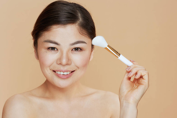 modern asian woman with makeup brush against beige background. - Фото, зображення