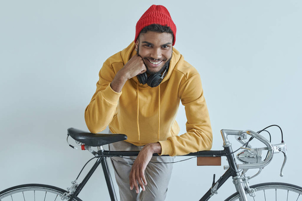 Handsome African man leaning at his bicycle and smiling while standing against the wall - Φωτογραφία, εικόνα