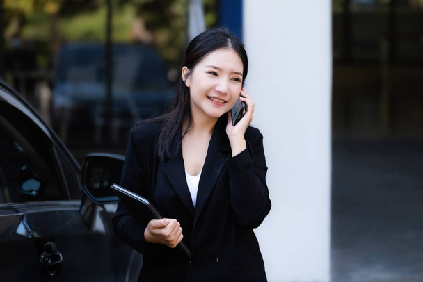 Asian businessmen, business owners, company presidents or female employees talking on the phone and holding a tablet are getting out of the car to attend a business plan meeting at the meeting - Foto, imagen