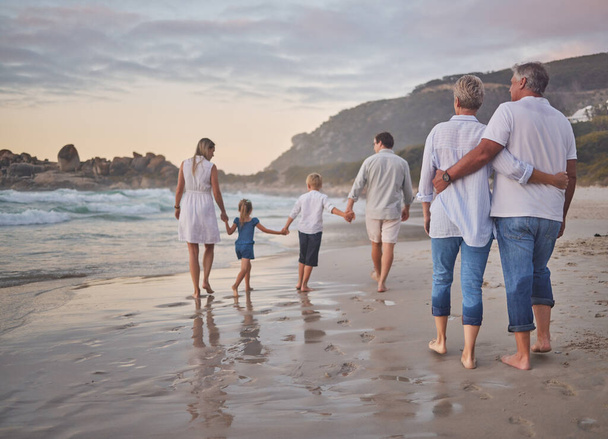 Zadní pohled na vícegenerační rodinu držící se za ruce a kráčející podél pláže společně. Kavkazská rodina se dvěma dětmi, dvěma rodiči a prarodiči si užívají letní prázdniny. - Fotografie, Obrázek