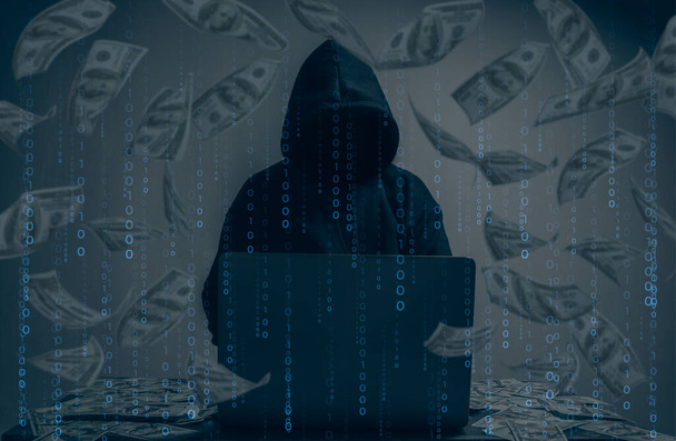 De hacker droeg een zwarte hoodie. Het stelen van enorme financiële gegevens op computers met binaire code digitale interface en veel dalende dollars en liggen op de tafel.Hacking en malware concept. - Foto, afbeelding