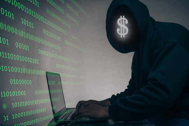 De hacker droeg een zwarte hoodie. Het stelen van enorme financiële gegevens op computers met binaire code digitale interface en veel dalende dollars en liggen op de tafel.Hacking en malware concept. - Foto, afbeelding