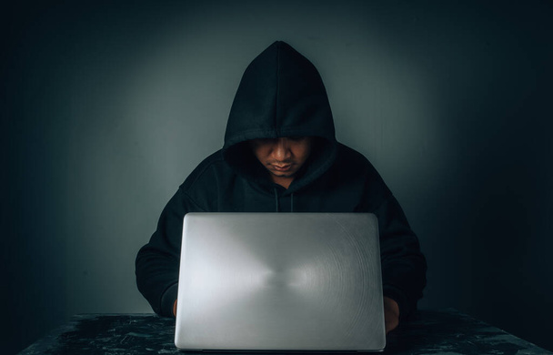 Hacker nosí košili s dlouhým rukávem a kapucí zakrývající jeho hlavu. Sedět v temné místnosti s notebookem Koncept krádeže identity v síti internetového tábora. s mezerou pro kopírování. - Fotografie, Obrázek