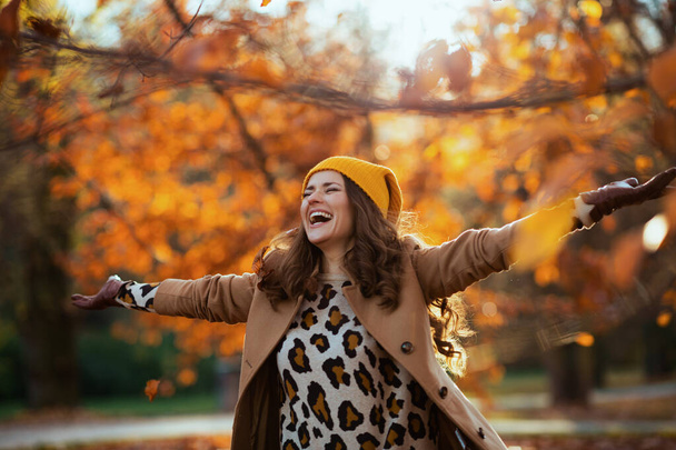 Hello september. happy young woman in brown coat and yellow hat rejoicing outside on the city park in autumn. - Foto, immagini